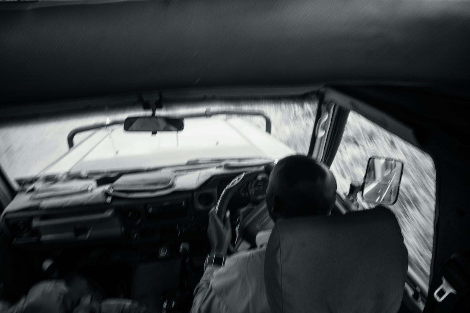 Black and white image of a man driving with a view of the car interior
