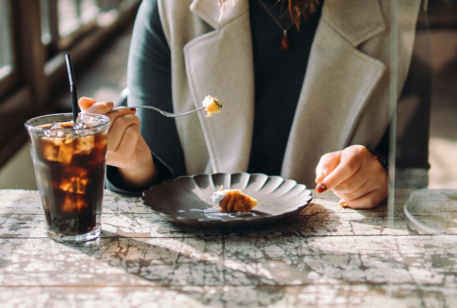 女性在桌子上吃甜點時手握甜點叉子和飲料