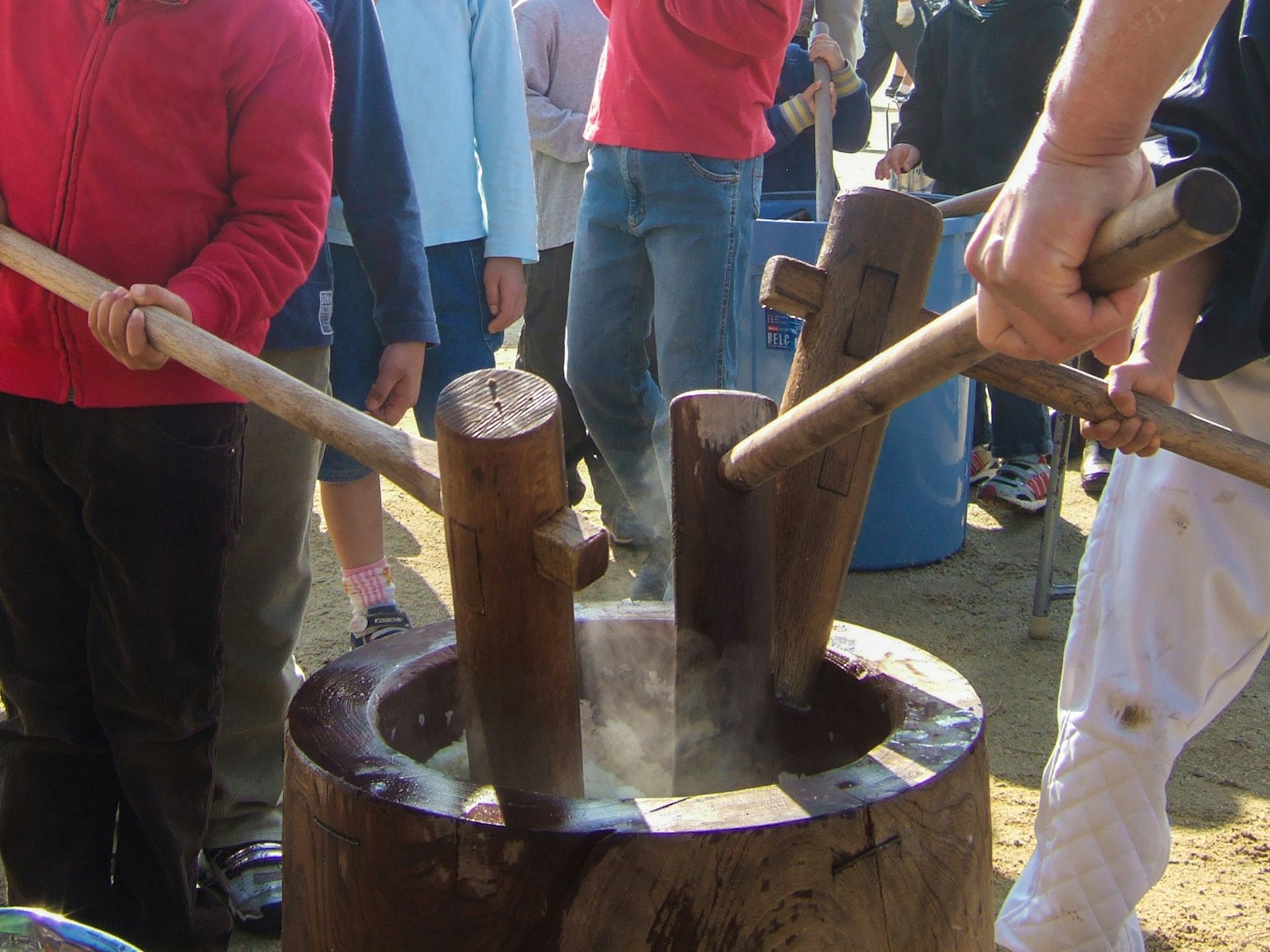 Personas golpeando pasteles de arroz con mazos de madera vapor que sale del mortero