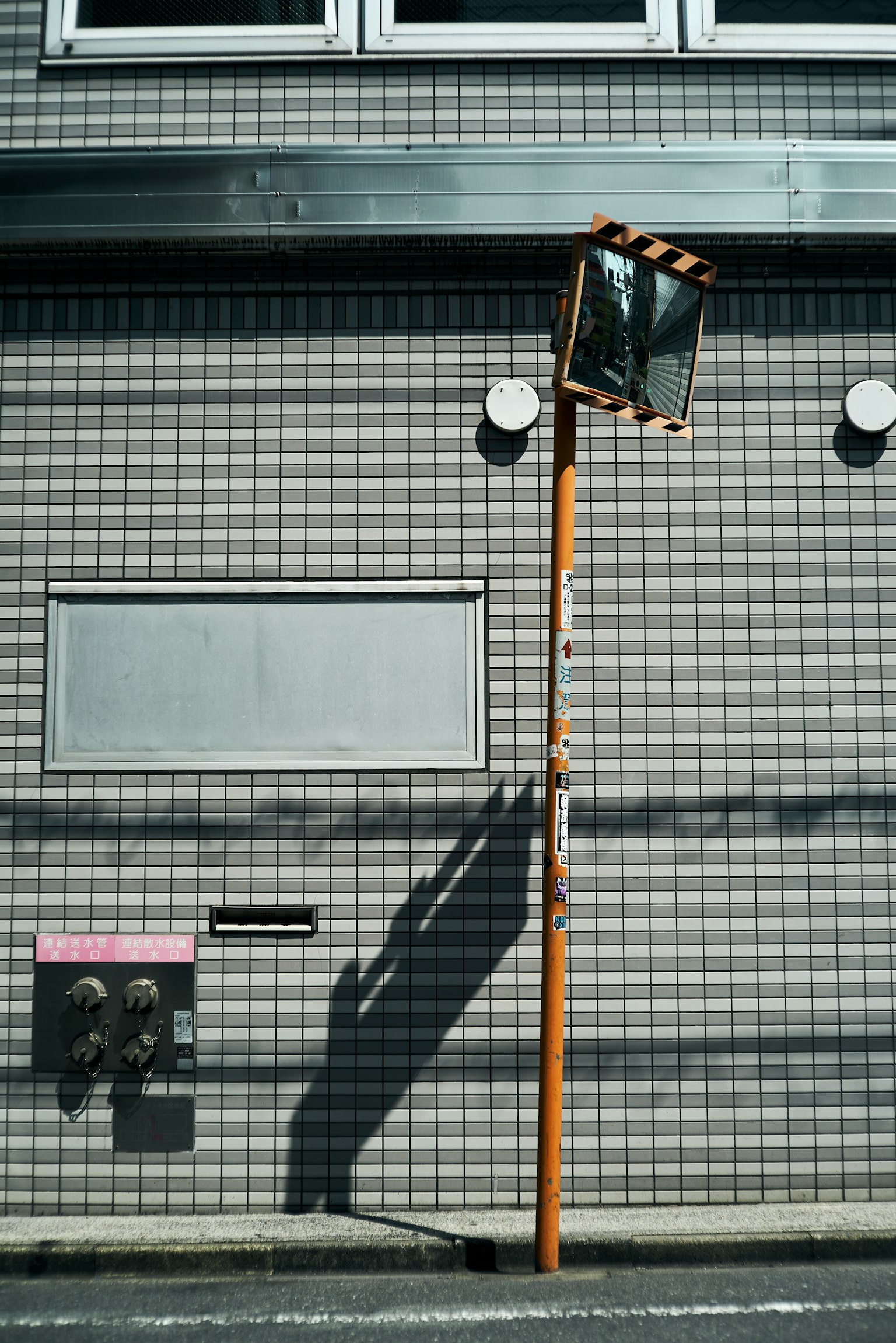 Poteau orange avec un miroir projetant une ombre sur un mur carrelé