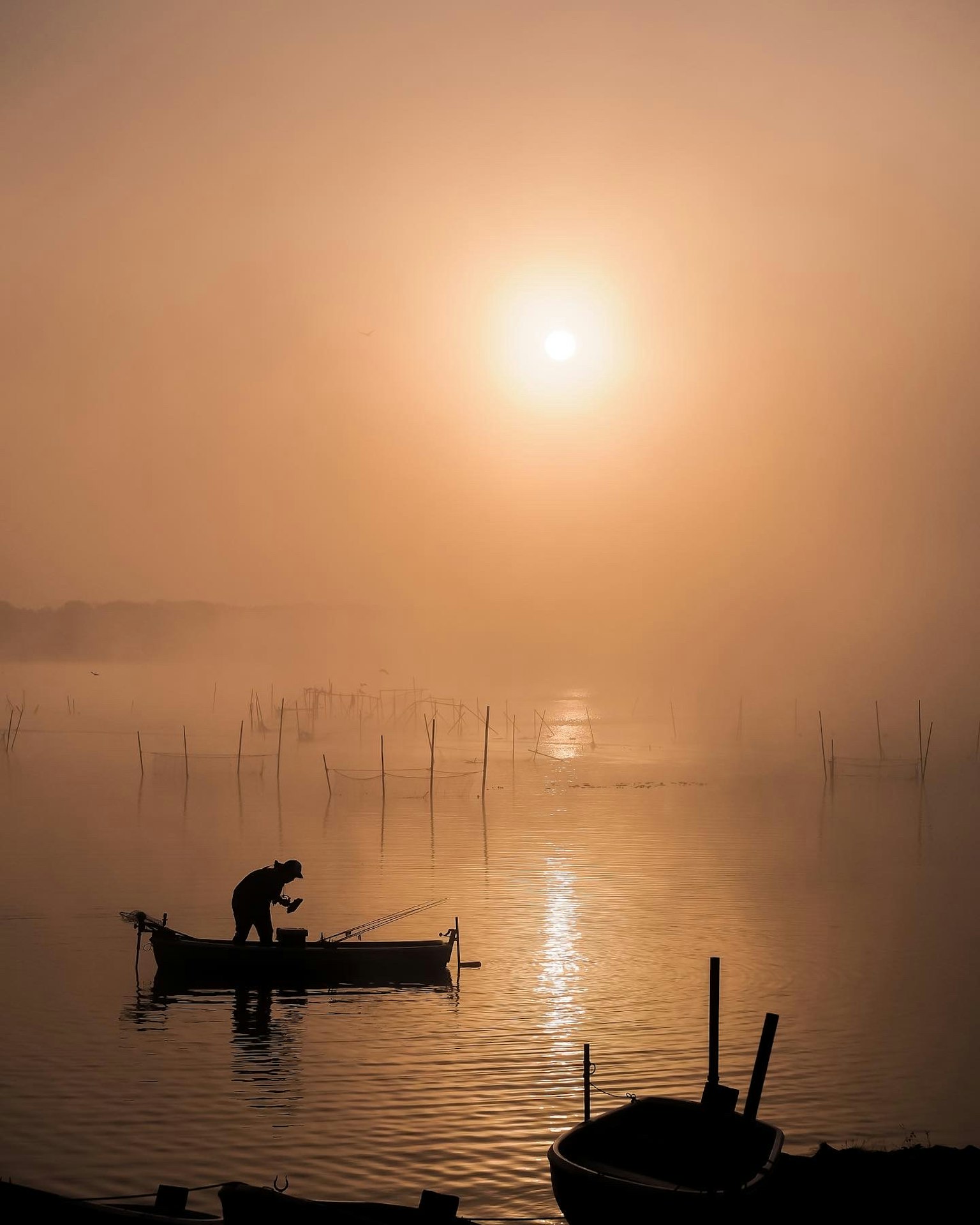 A person fishing in a boat with a stunning sunset in a foggy landscape