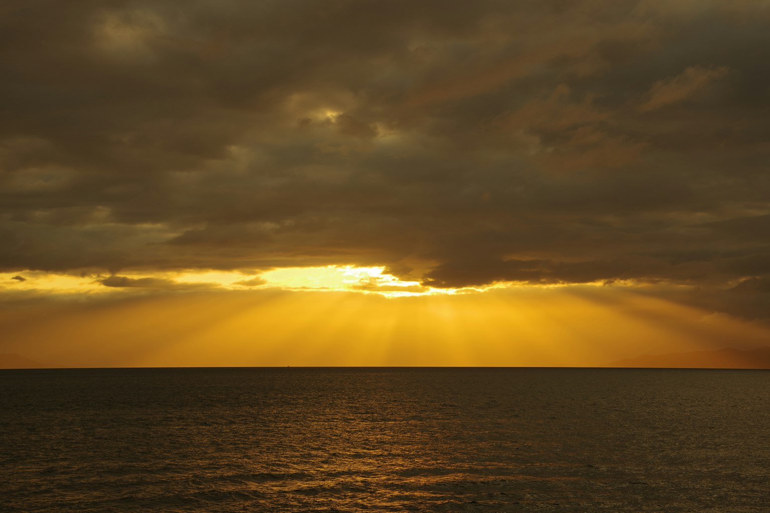 Sunset over the ocean with rays of light breaking through clouds