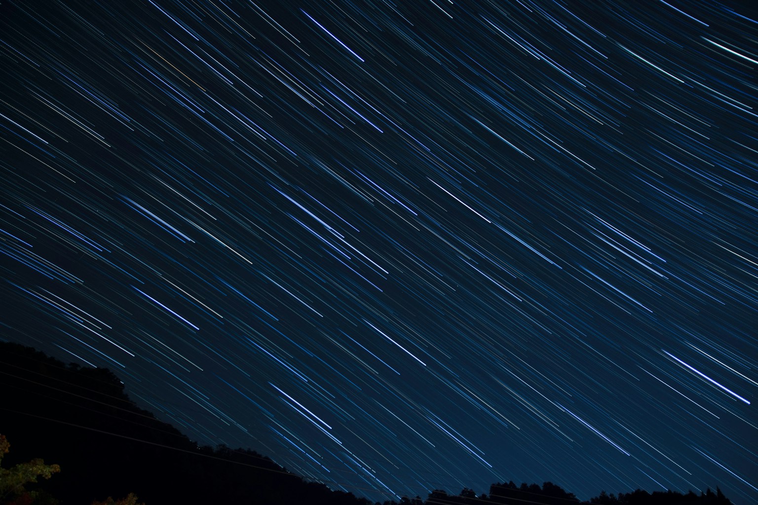 Traînées d'étoiles dans un ciel nocturne sombre avec des silhouettes de montagnes