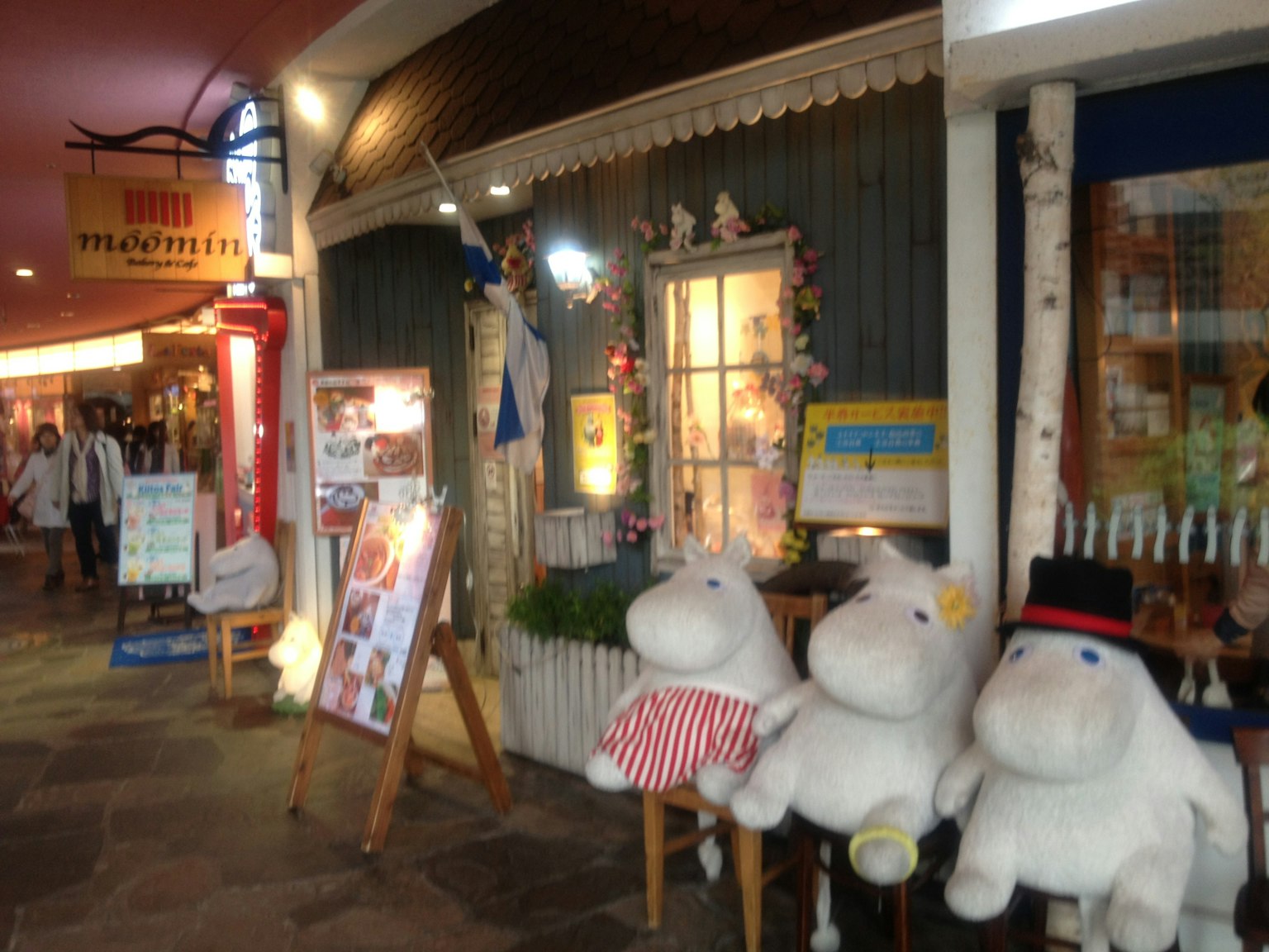 Exterior de un café con peluches Moomin y luz cálida desde la ventana
