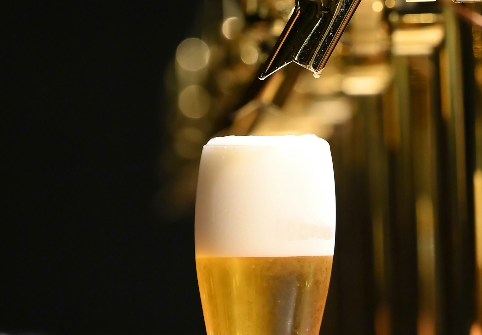 Glass of beer with frothy head and beer tap in the background