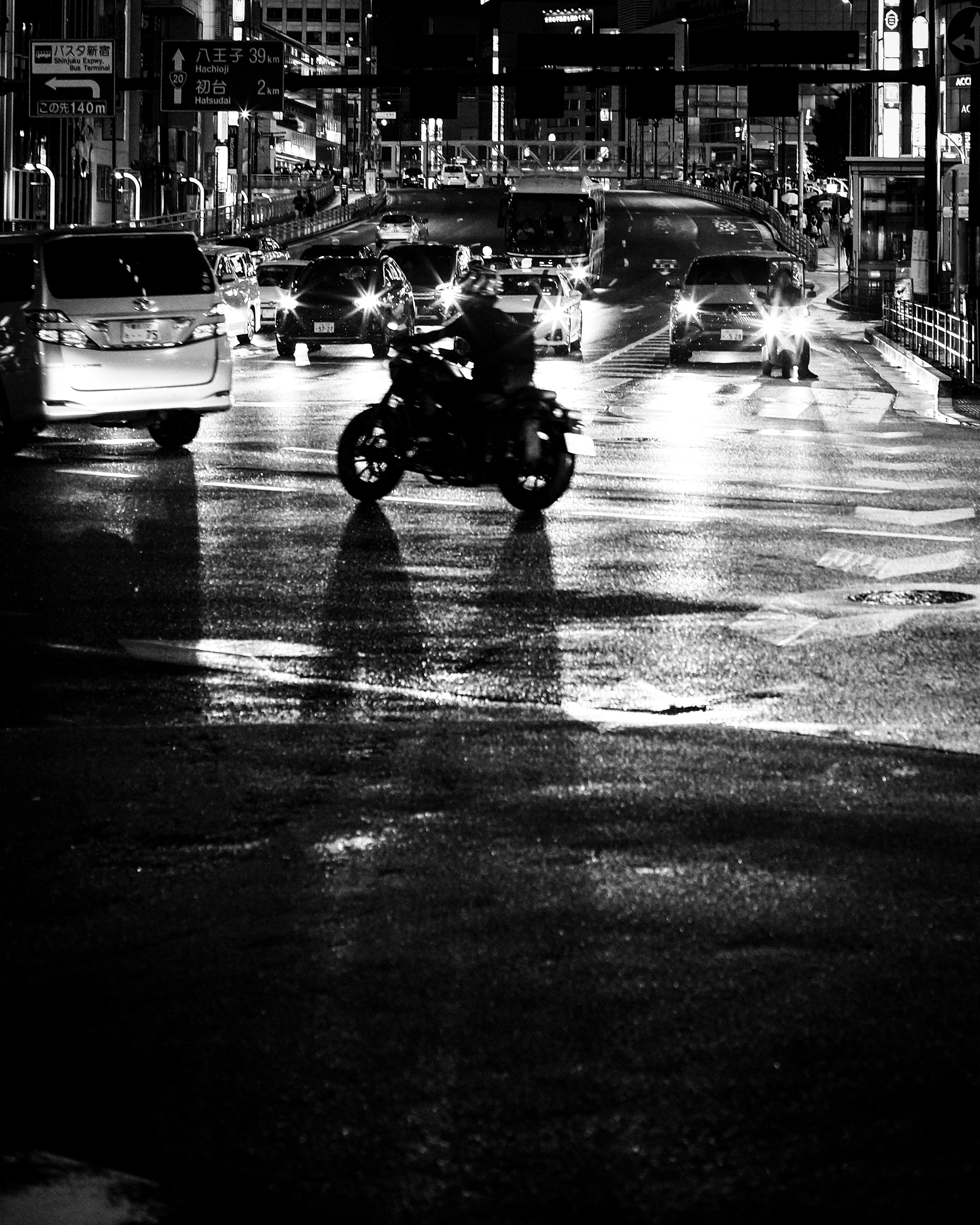 雨上がりの夜の交差点で走るバイクと車の光