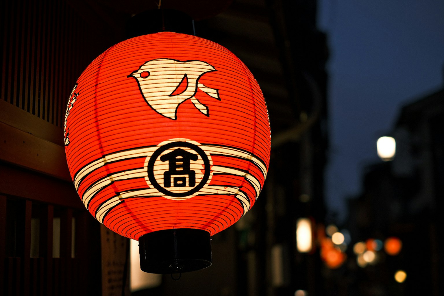 Rote Laterne mit einem weißen Vogeldesign und Kanji-Logo in einer nächtlichen Straßenumgebung