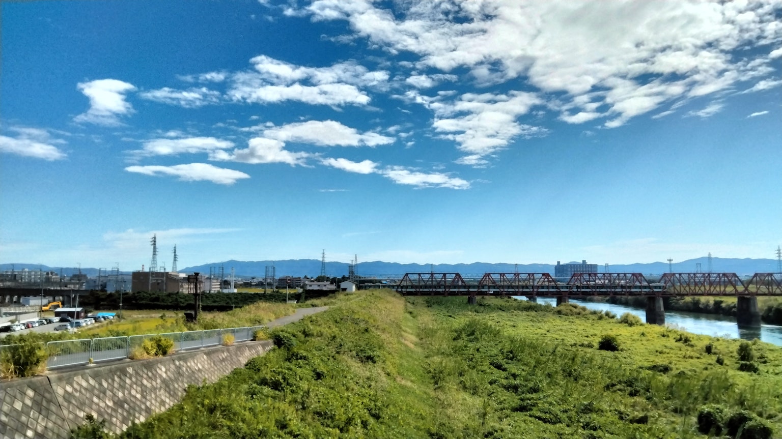 Pemandangan dengan langit biru dan awan rumput hijau dan sungai mengalir jembatan dan pabrik terlihat