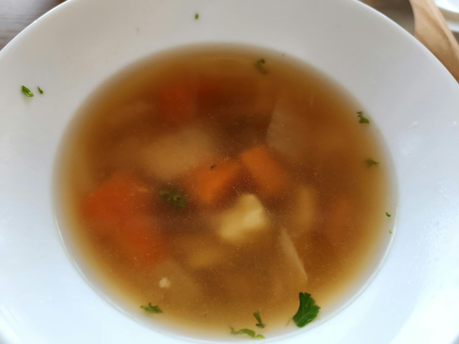 Un bol blanc rempli de bouillon clair avec des légumes en dés comme des carottes et des herbes