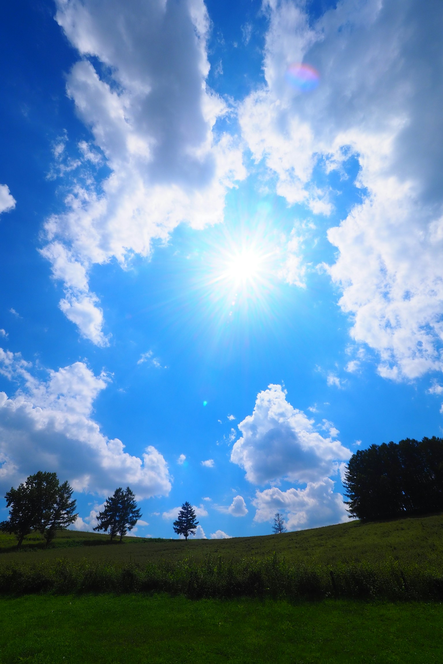 Eine Landschaft mit blauem Himmel und weißen Wolken strahlender Sonne über grünen Hügeln