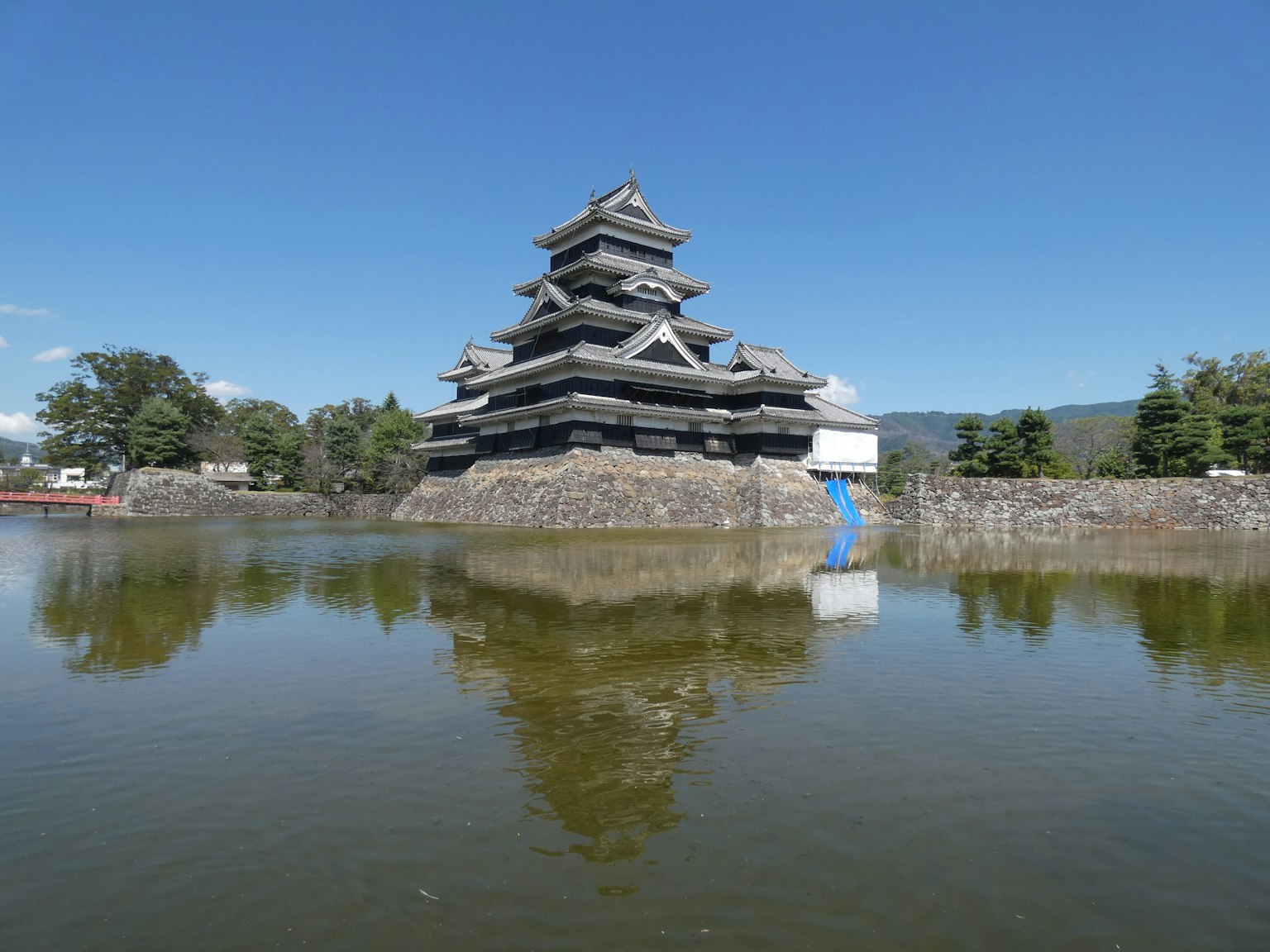 Eksterior menakjubkan Kastil Matsumoto yang tercermin di air di bawah langit biru yang cerah
