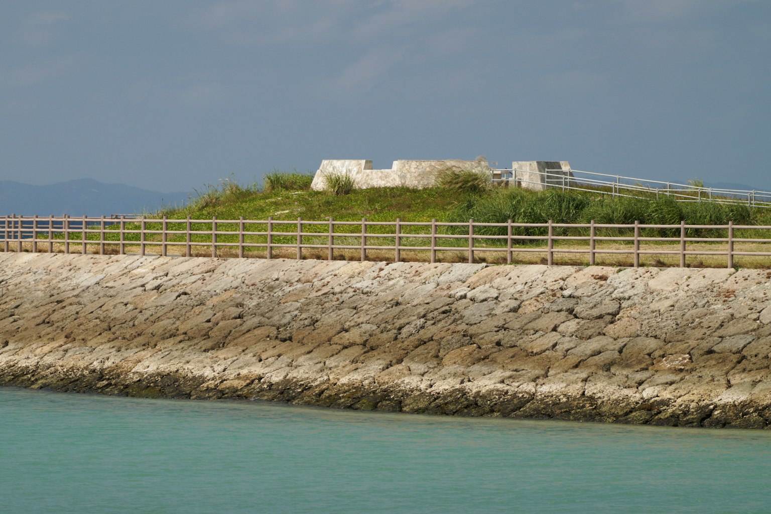 Steinmole, die dem Meer zugewandt, mit einer alten Festung auf einem grünen Hügel
