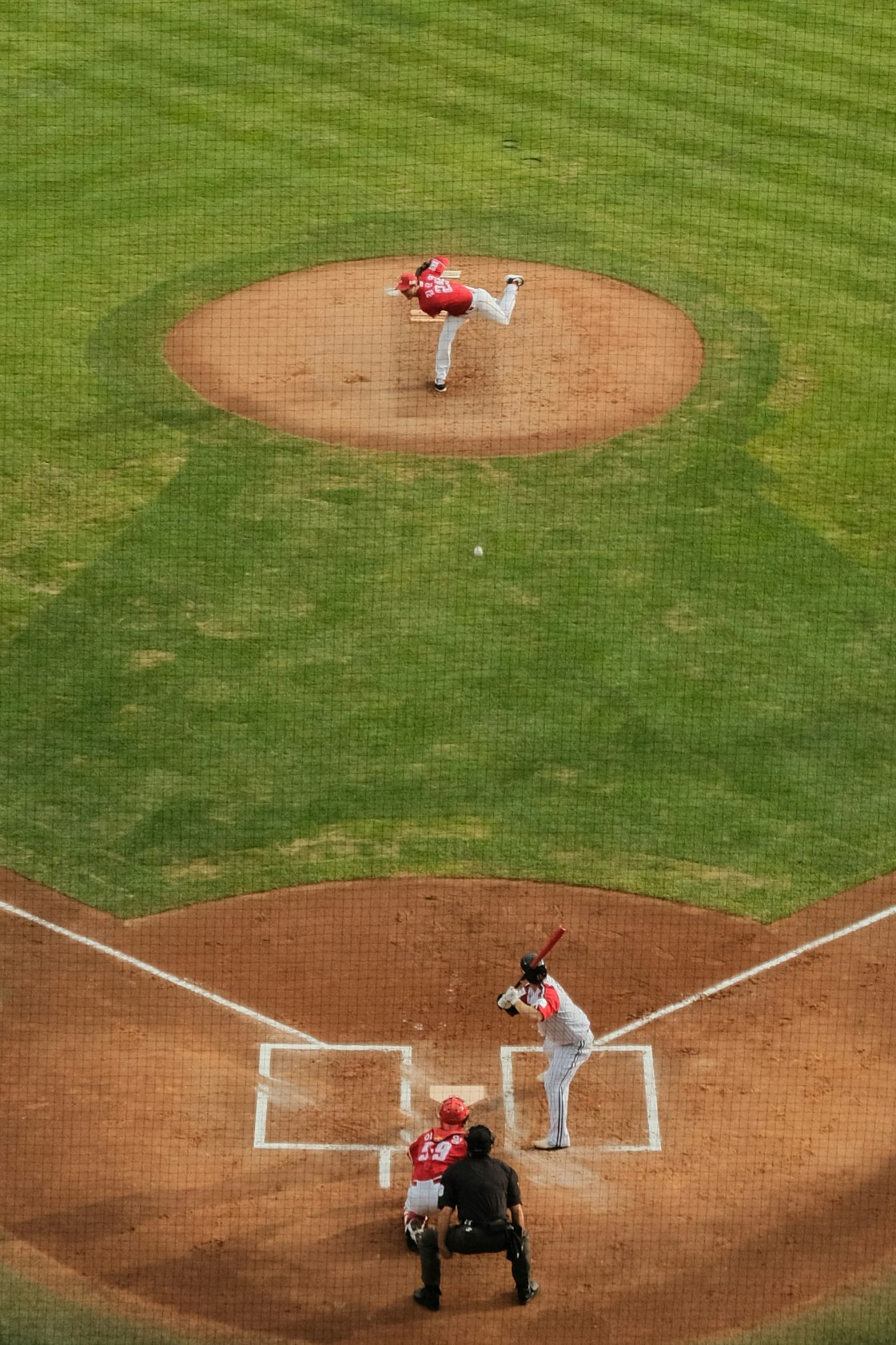 trận bóng chày với cầu thủ ném bóng đang ném và catcher phía sau home plate