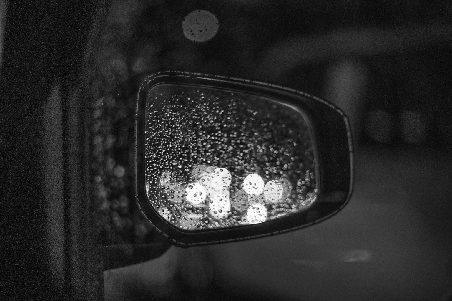 Specchietto laterale di auto bagnato dalla pioggia che riflette luci sfocate