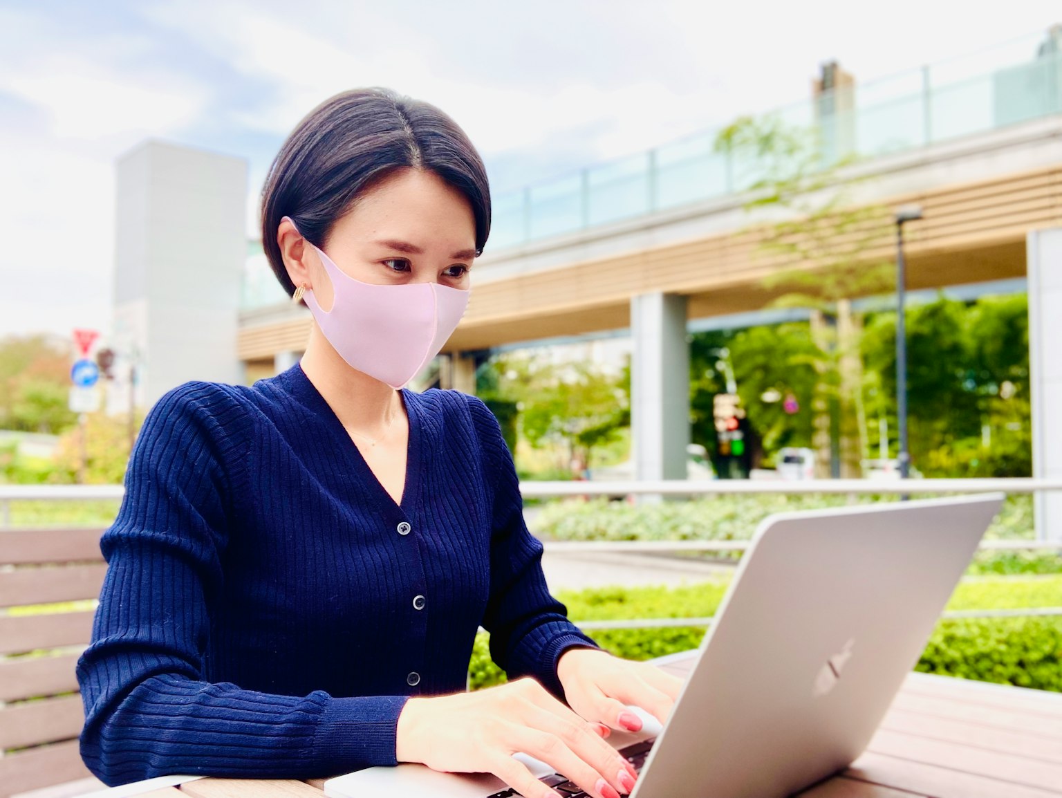 Frau mit Maske, die in einem Park an einem Laptop arbeitet