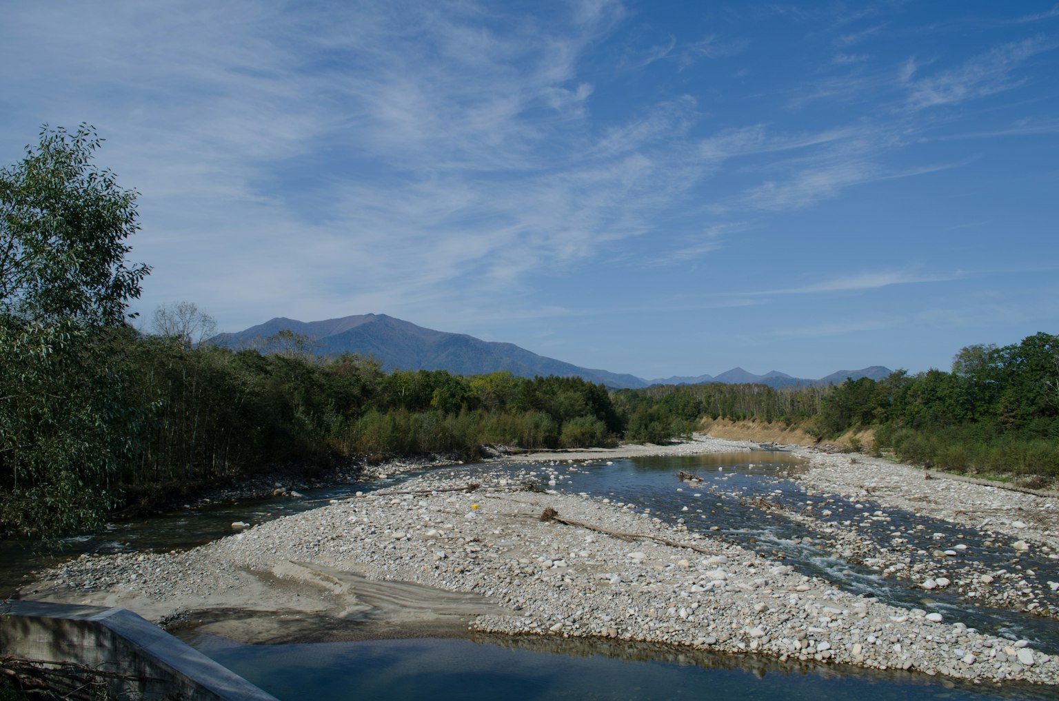 Paesaggio fluviale sotto un cielo blu con montagne riva rocciosa e alberi verdi