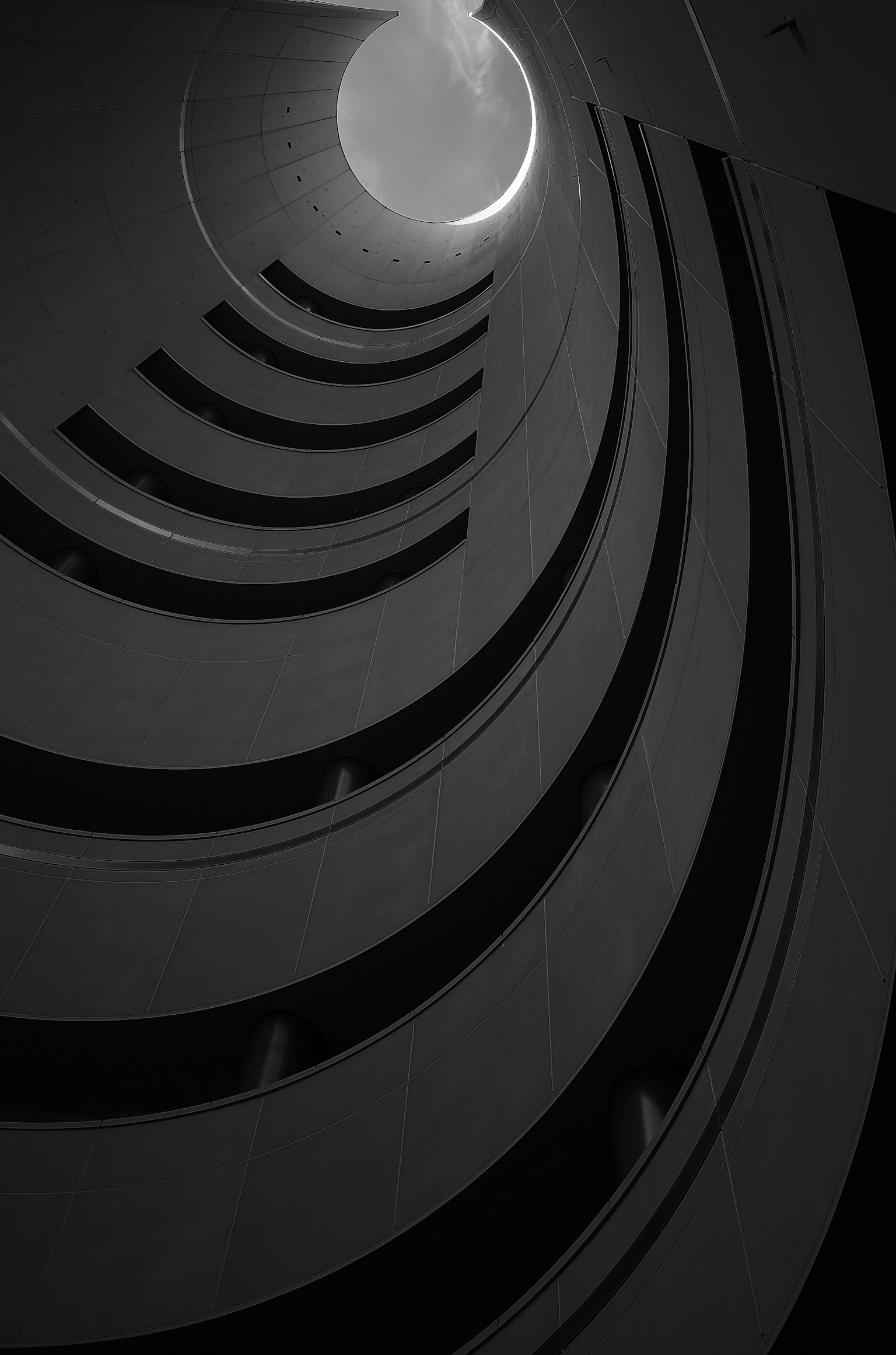 Monochrome photo looking up a spiral staircase Bright light coming from above