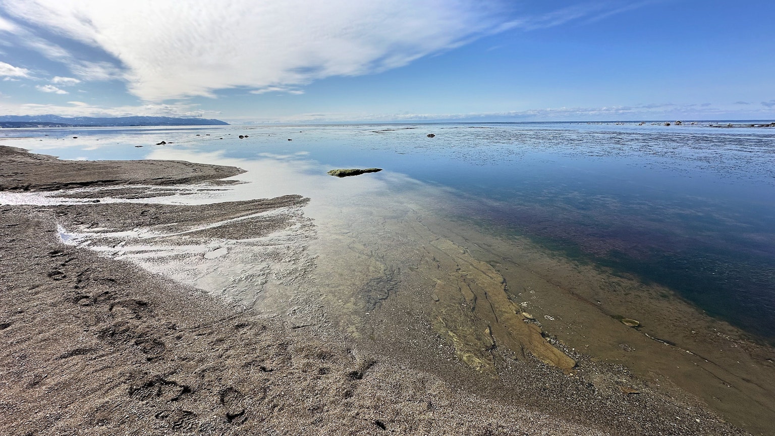 Ruhige Strandlandschaft mit blauem Himmel und Wolkenreflexionen auf dem Wasser