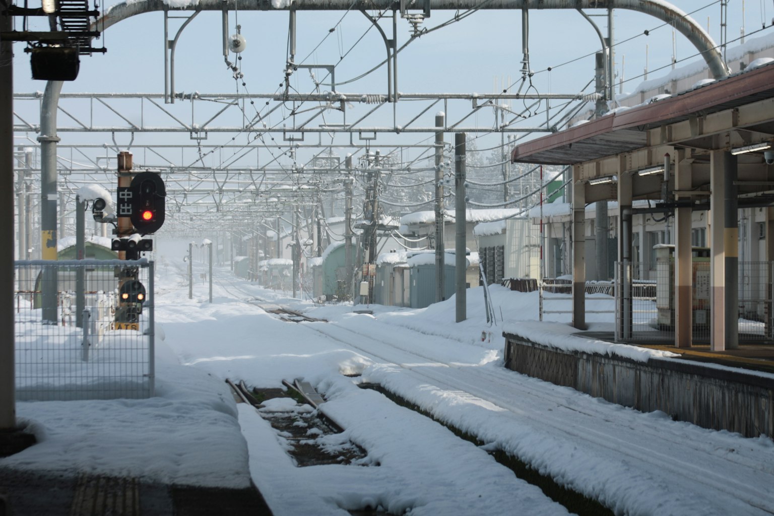 Gare enneigée avec des rails visibles feu de signalisation et fils aériens