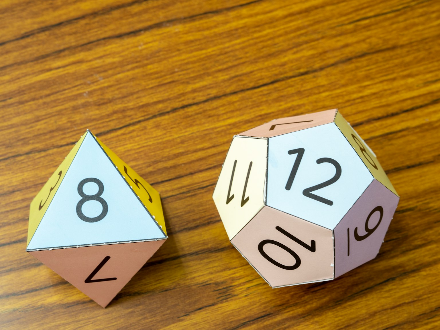 Dos dados están sobre una mesa de madera Uno es un tetraedro con el número 8 y el otro es un dodecaedro con el número 12