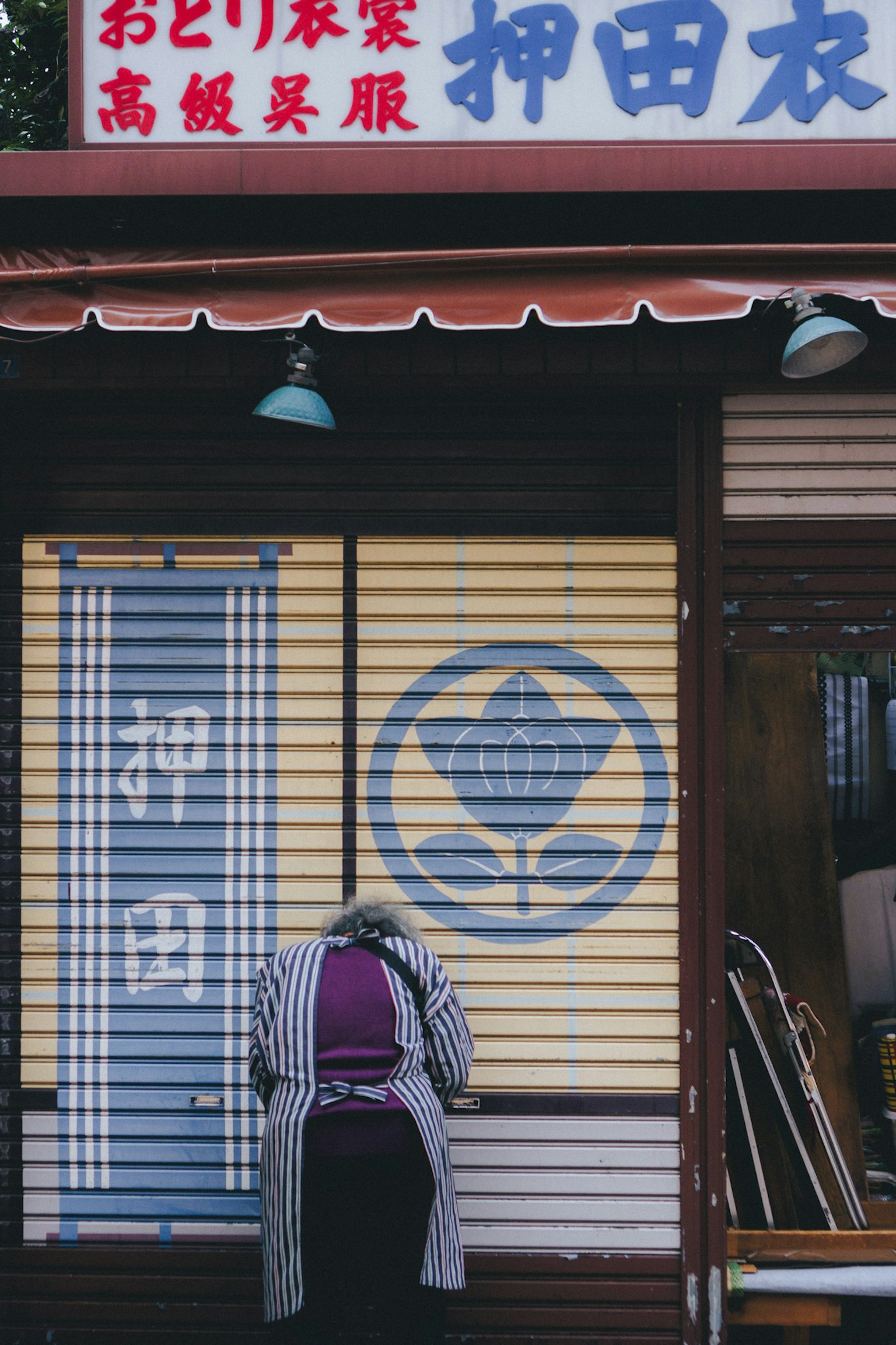 Eksterior toko tradisional Jepang dengan tanda biru dan pola putih serta seseorang yang bekerja di depannya
