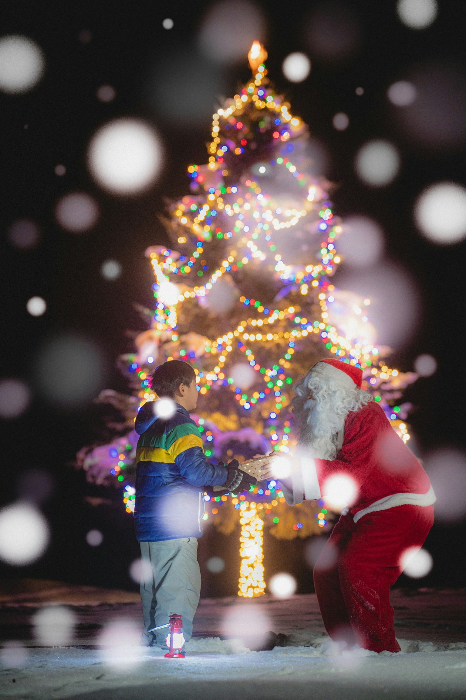 Un enfant et le Père Noël s'amusent devant un sapin de Noël décoré dans la neige