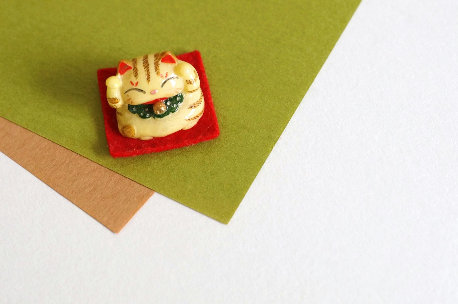 A cat figurine placed on a red mat atop green and brown paper