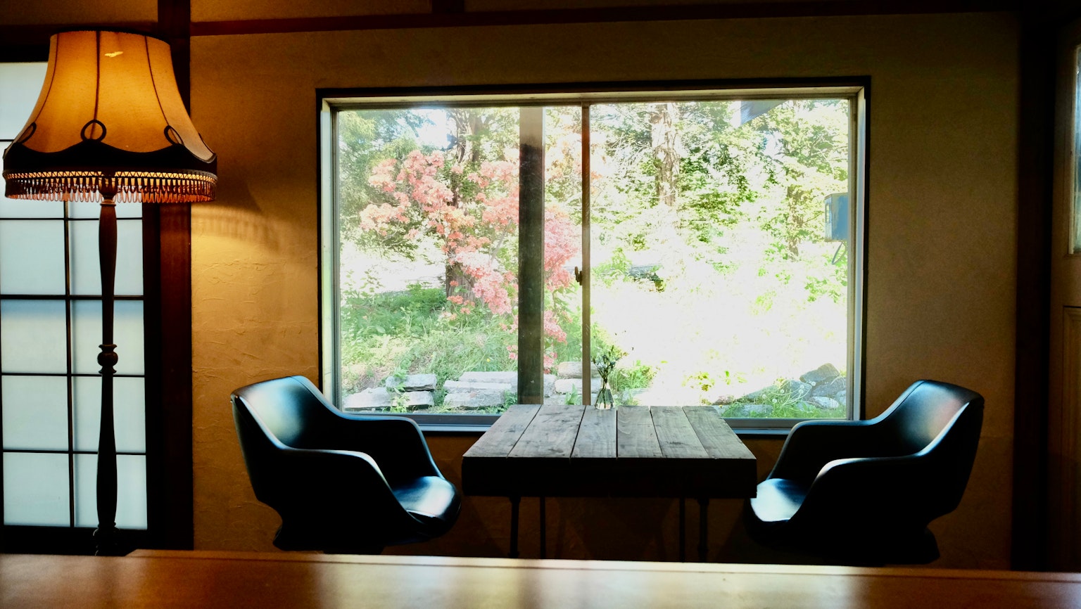 Ein gemütlicher Raum mit einem Holztisch und zwei Stühlen neben einem großen Fenster mit Blick auf einen Garten