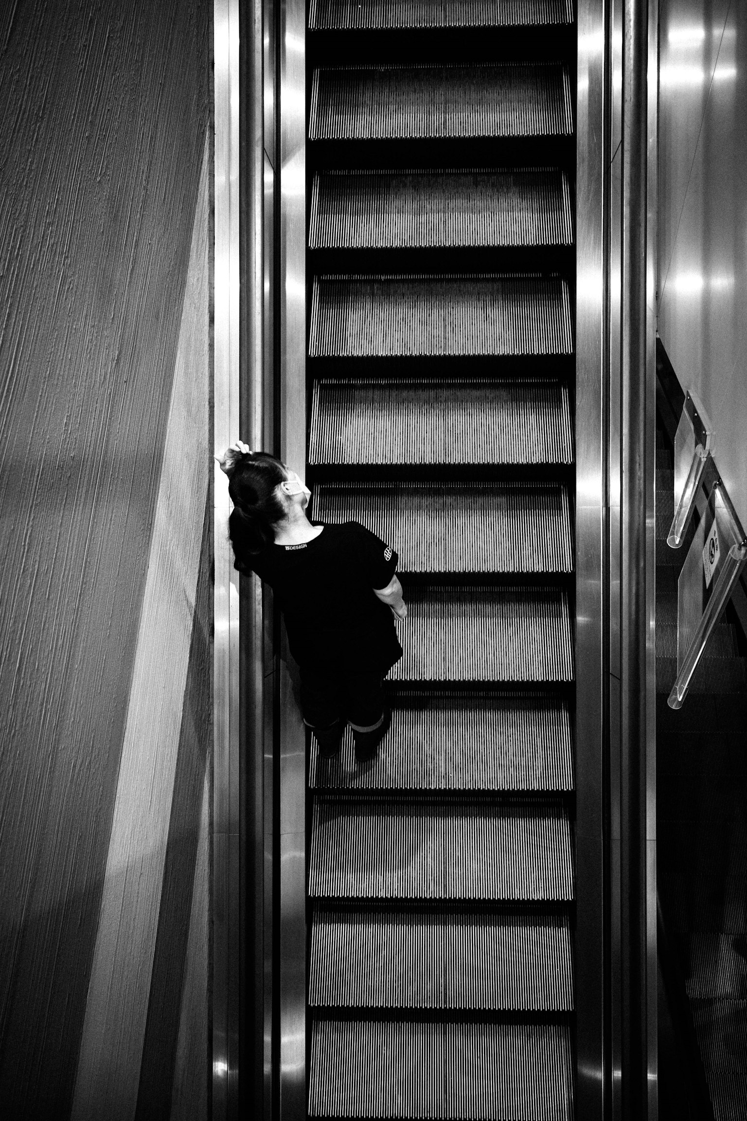 Foto hitam putih seorang wanita di eskalator dari atas