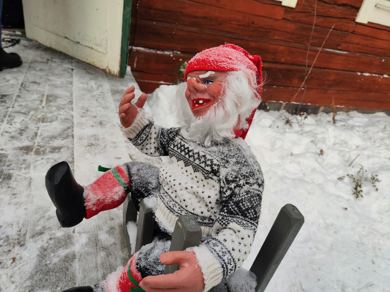 Einzigartige Puppe im Schnee sitzend mit rotem Hut und weißen Haaren und fröhlichem Gesichtsausdruck