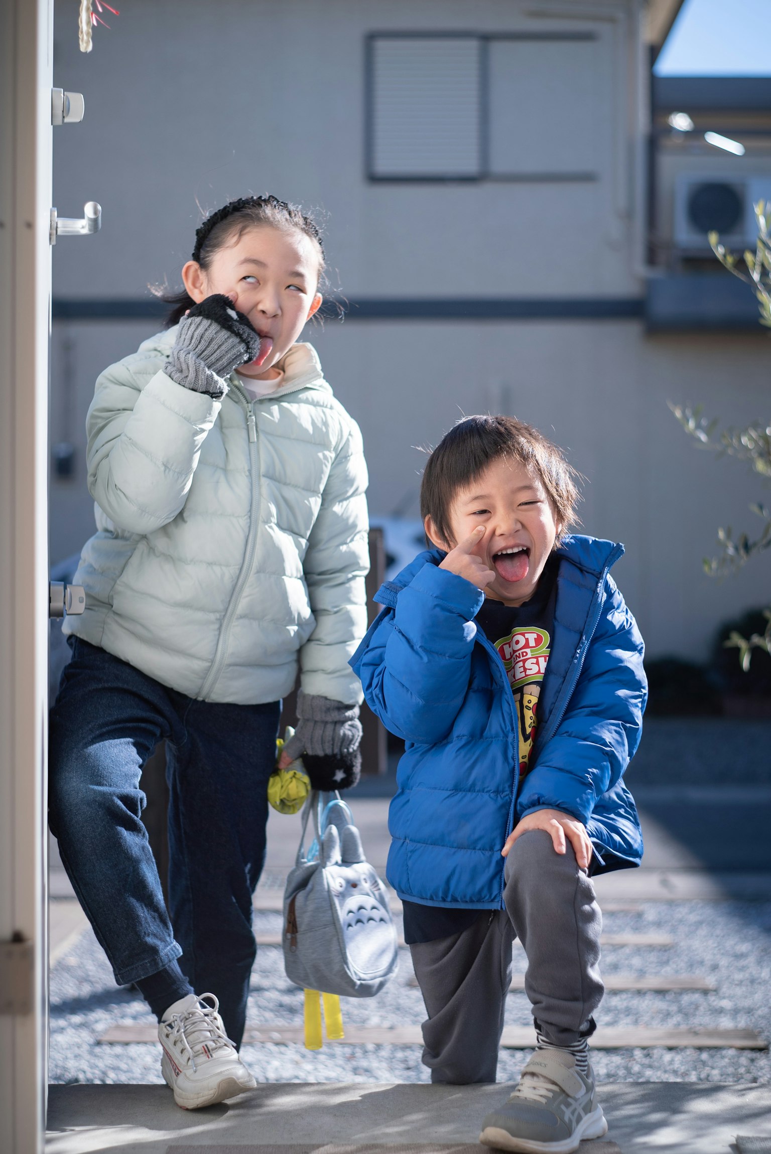 Dos niños jugando afuera con un abrigo azul y un abrigo gris sonriendo felizmente