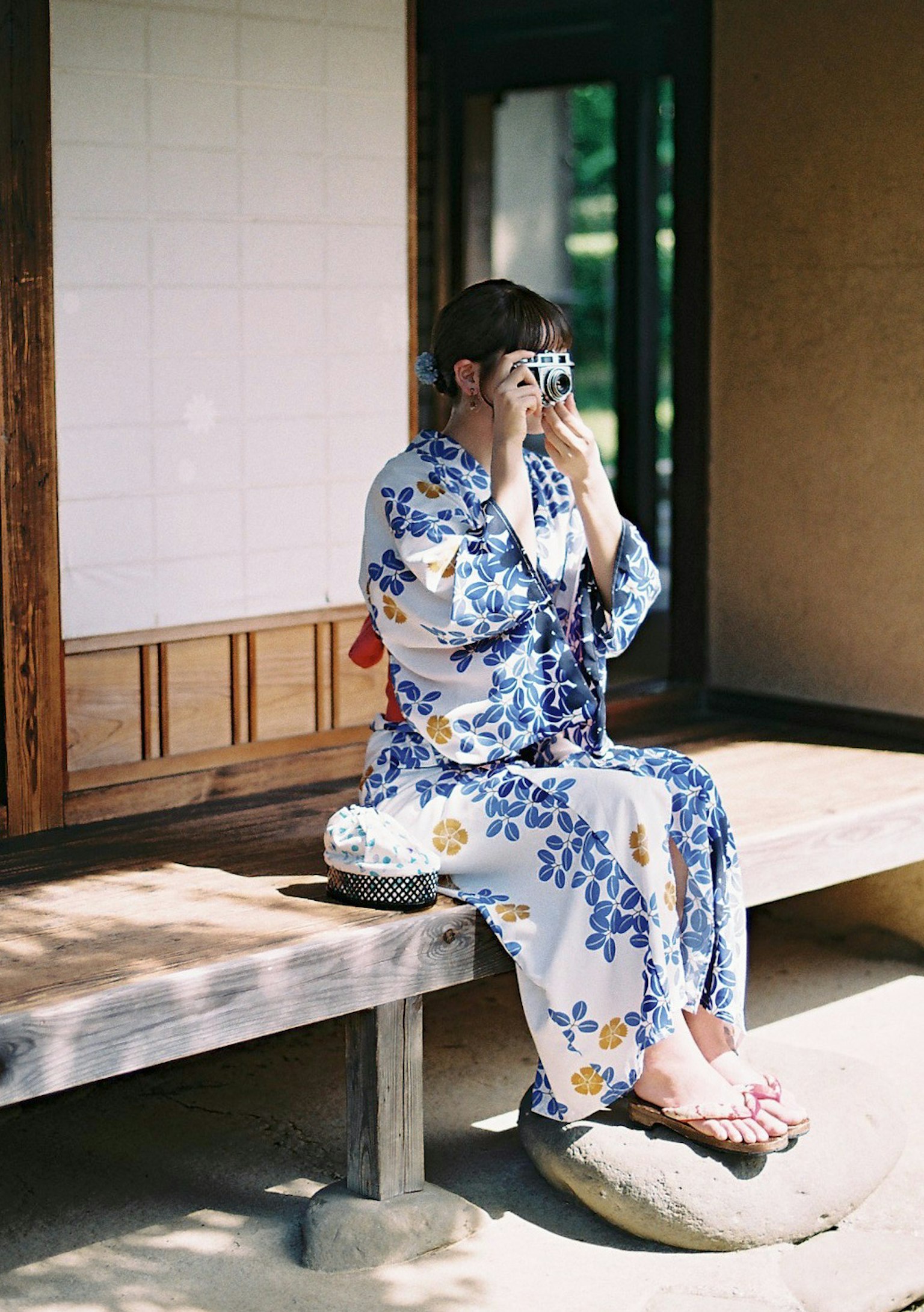 Femme en yukata floral bleu assise et tenant un appareil photo