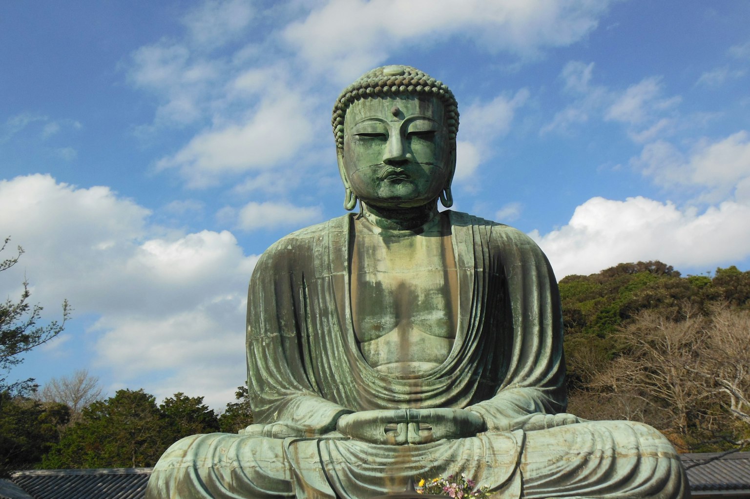 Statue de Bouddha en bronze assise avec un ciel bleu et des nuages en arrière-plan