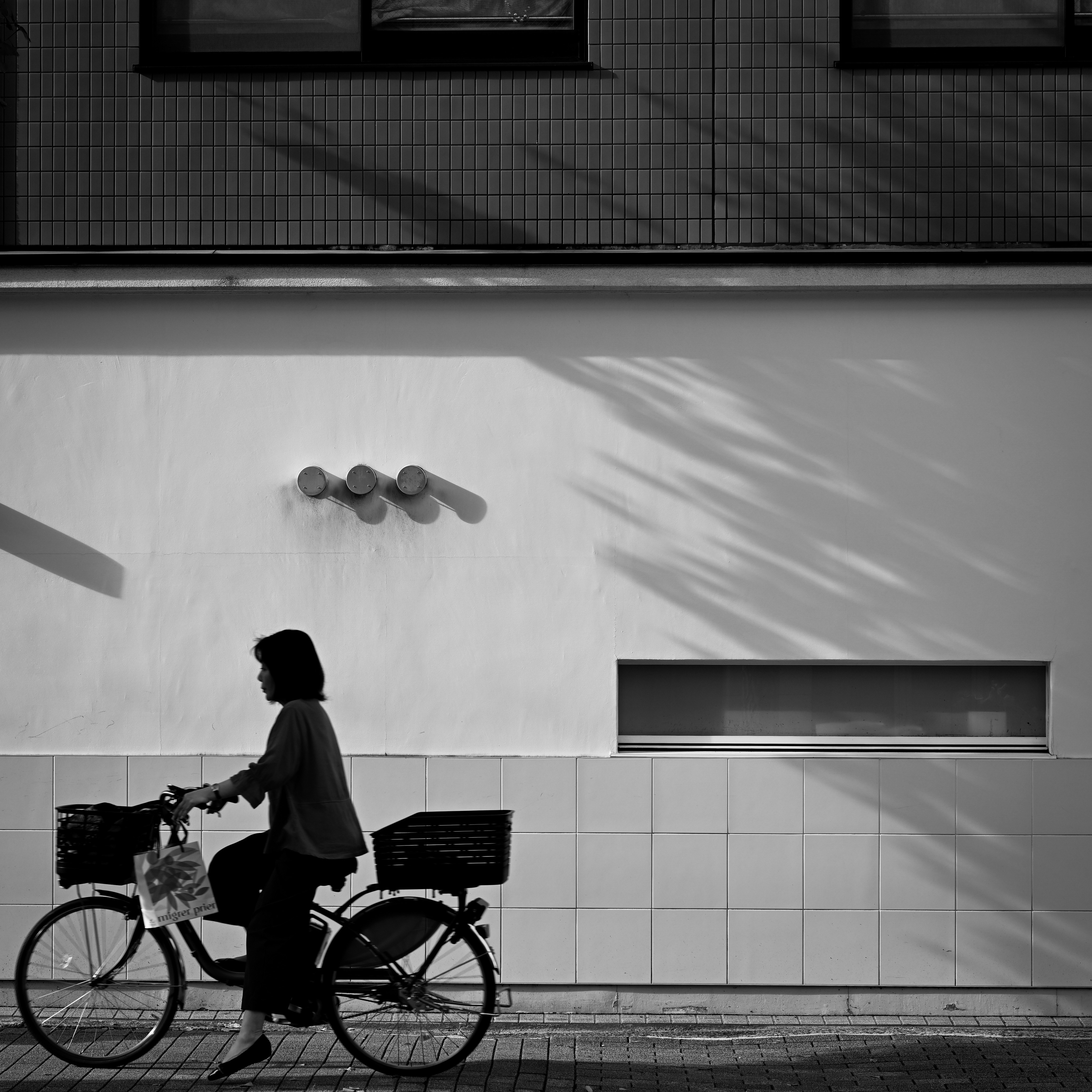 白壁の路地で自転車に乗る人のシルエットと斜光の影