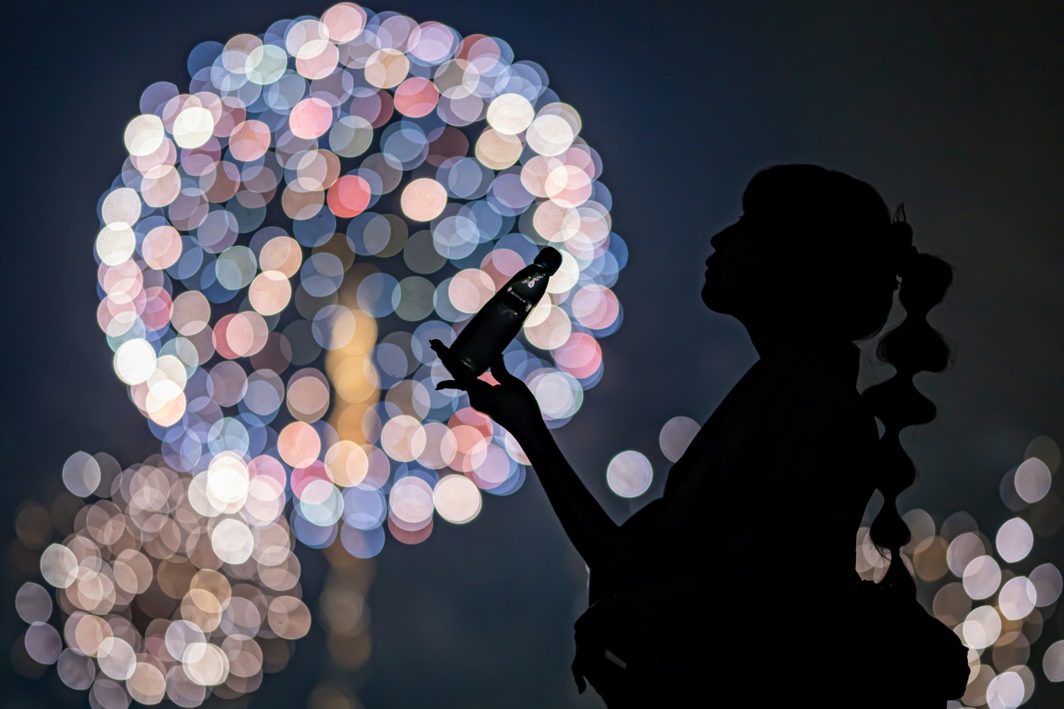 Silhouette of a woman holding a drink with fireworks in the background