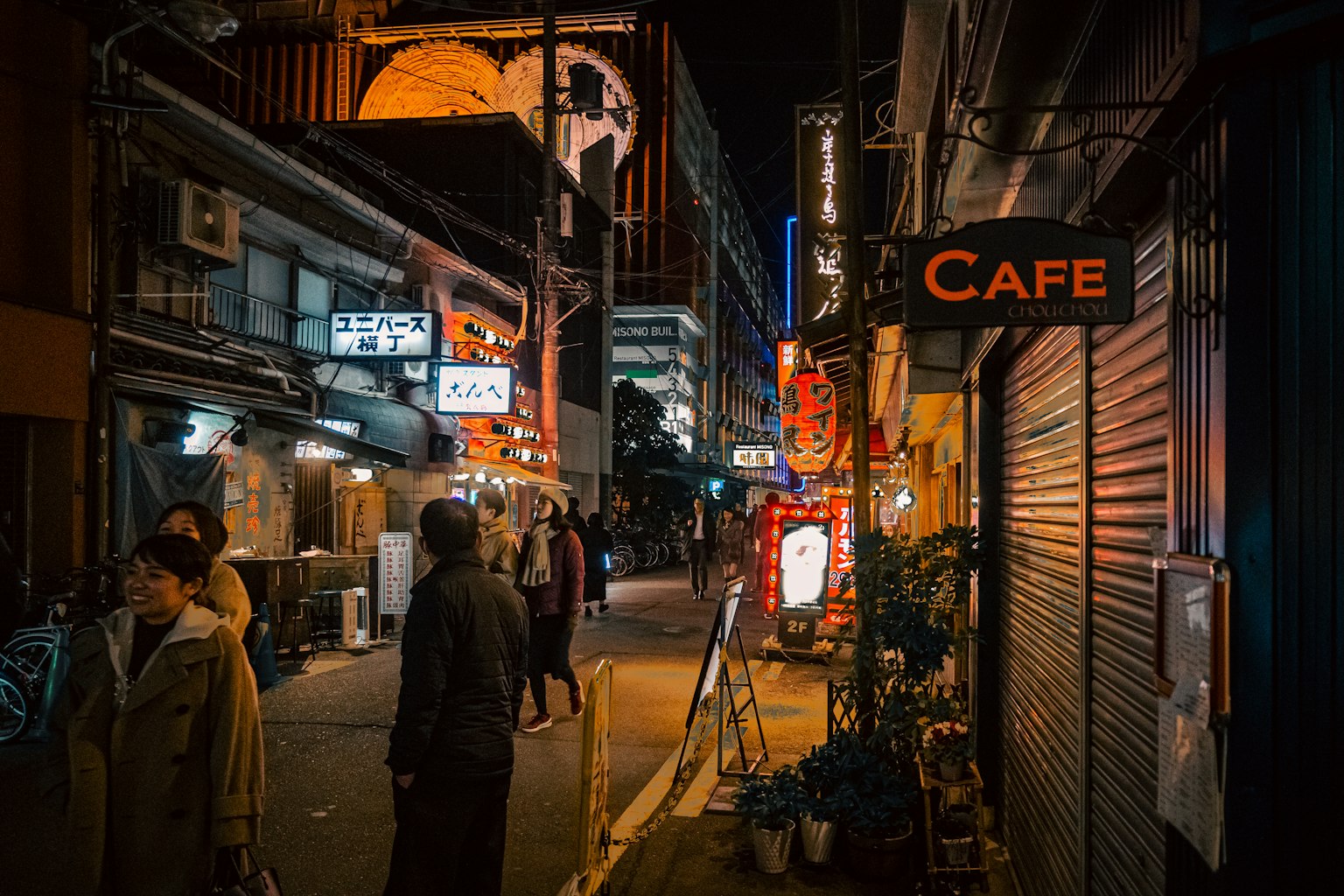 ฉากถนนยามค่ำคืนที่คึกคักมีป้ายร้านกาแฟและคนเดินถนน