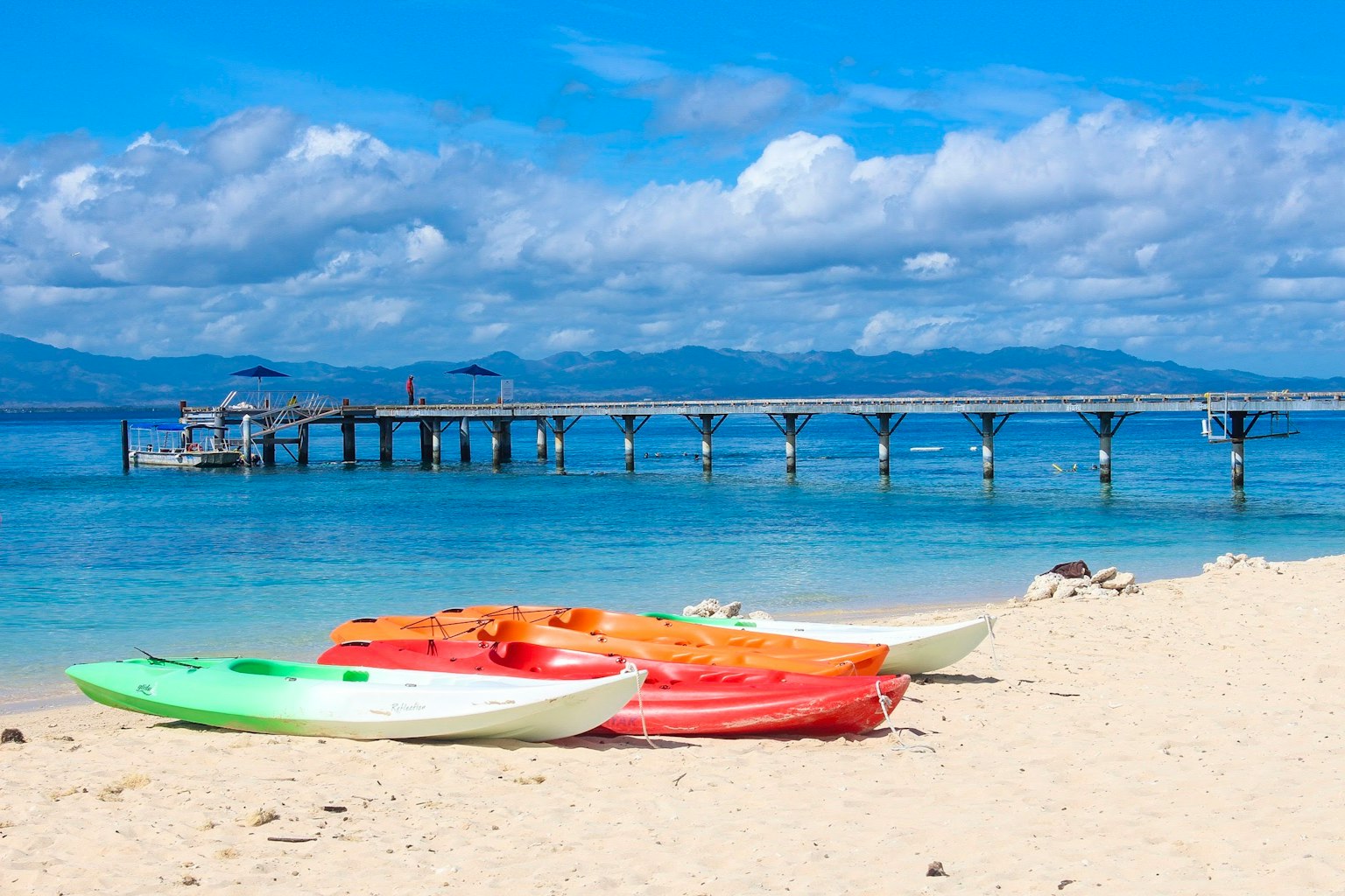 Pemandangan pantai dengan kayak berwarna di pasir dan dermaga kayu di latar belakang