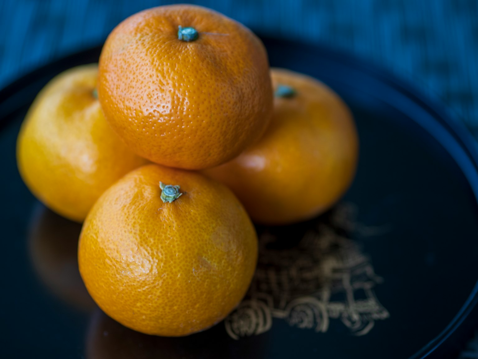 Four oranges stacked on a decorative plate with intricate design