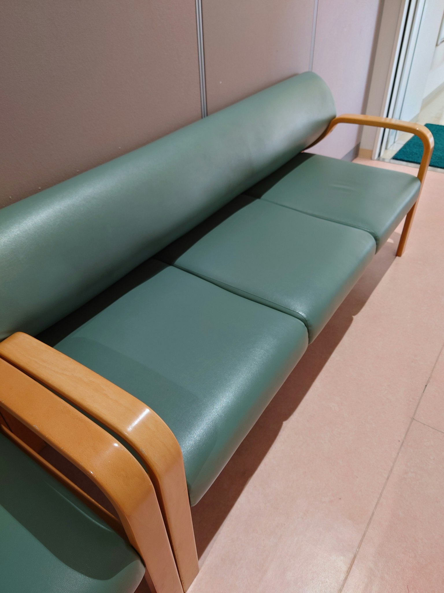 Detailaufnahme eines grünen Sofas mit Holzarmen und glatten Kissen