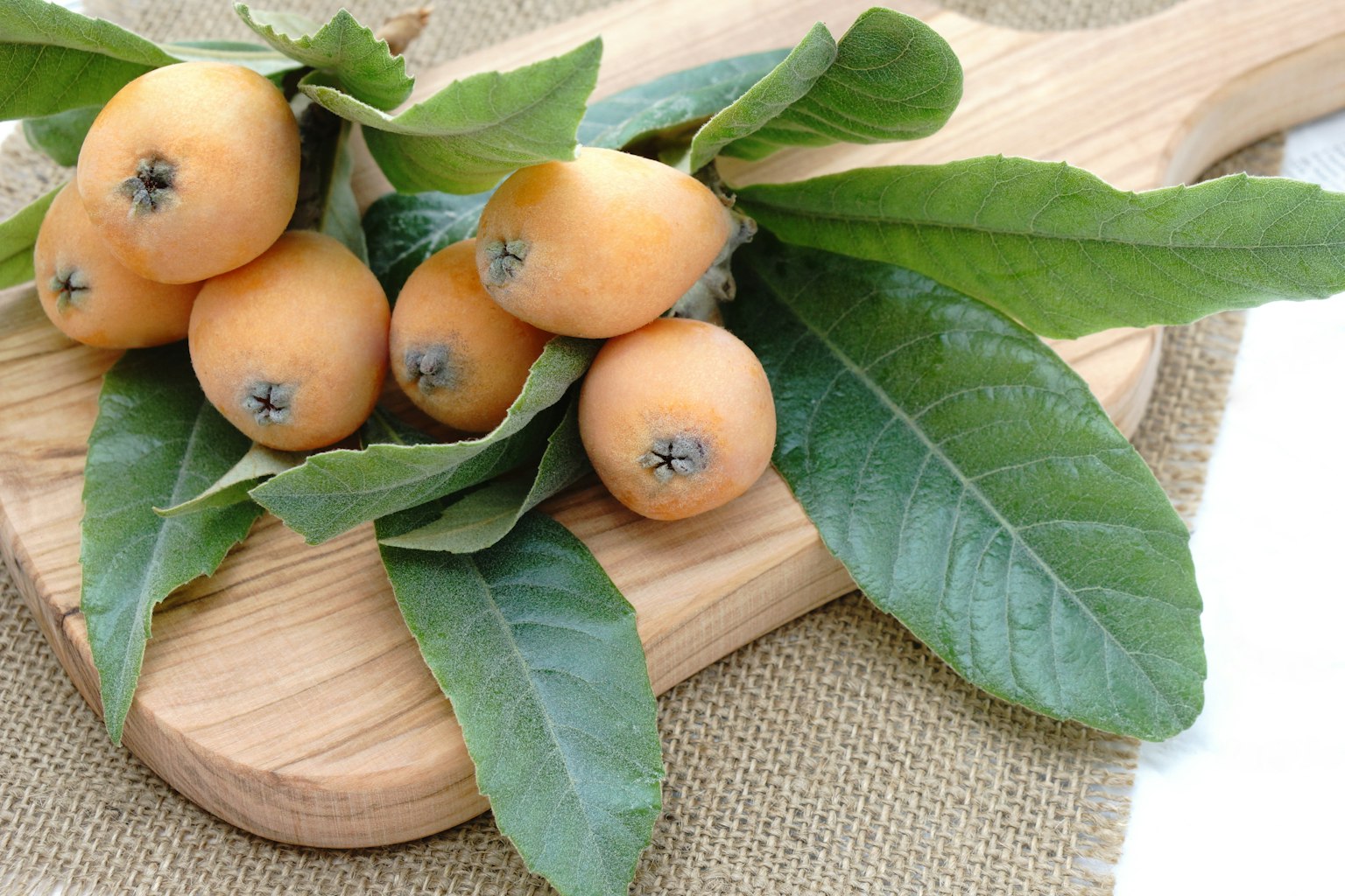 Loquats with green leaves on a wooden cutting board