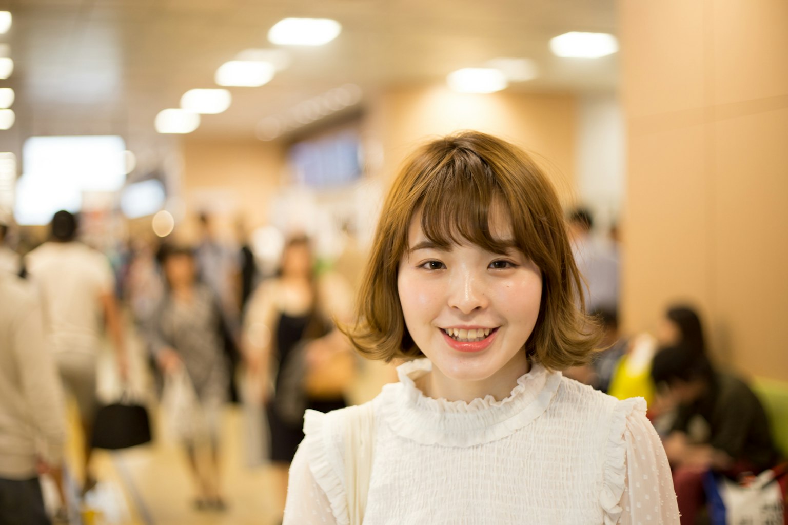 A smiling woman in a busy train station with people in the background