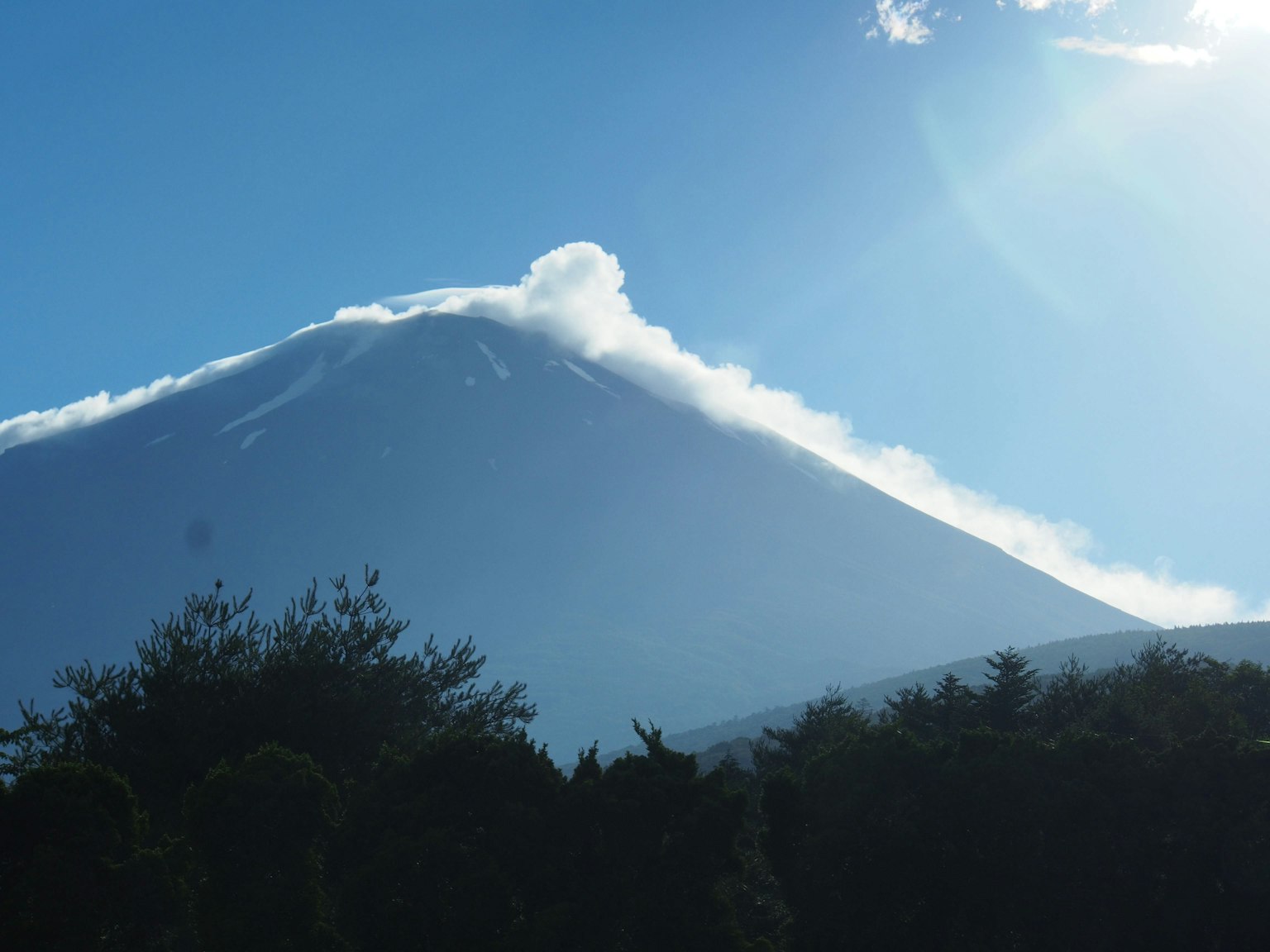 Gunung berapi mengeluarkan asap di bawah langit biru yang cerah