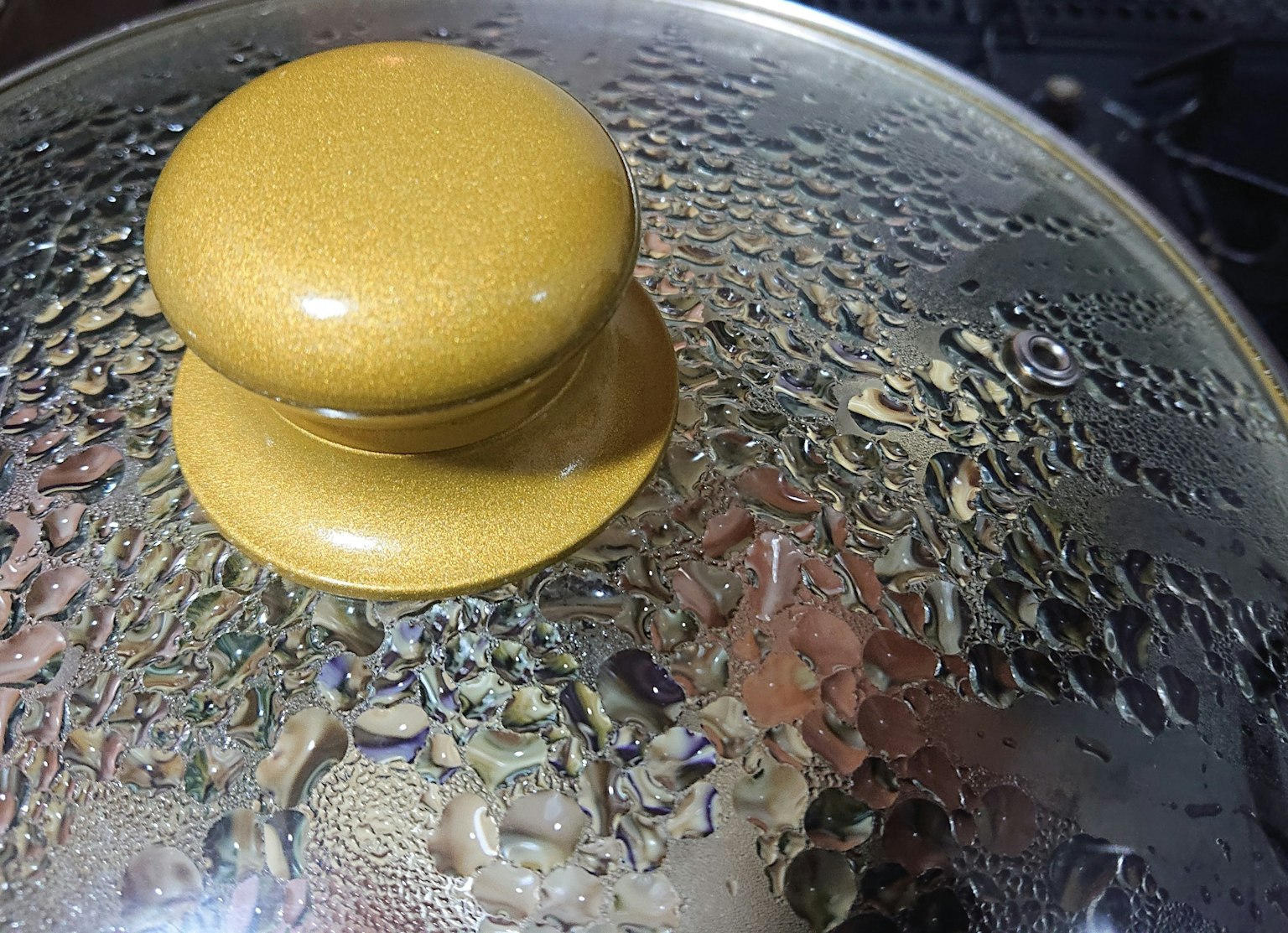 Gelber Knopf auf einem dampfenden Topfdeckel mit Wassertropfen