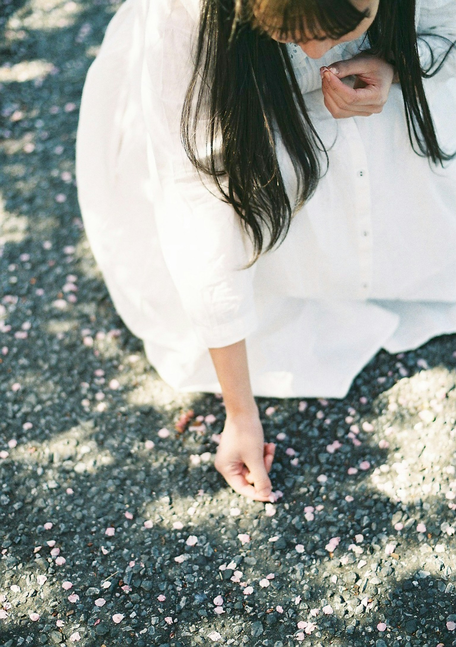 Una donna in abito bianco che raccoglie petali di fiori da terra