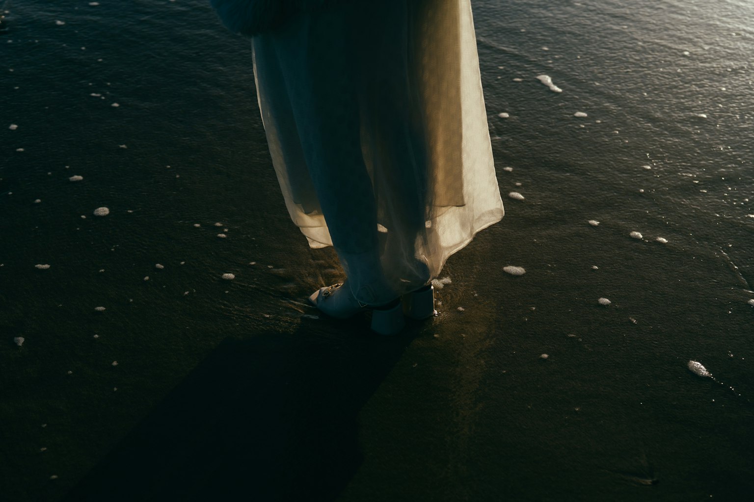 ผู้หญิงในชุดสีขาวยืนอยู่ที่ชายหาดสัมผัสคลื่น