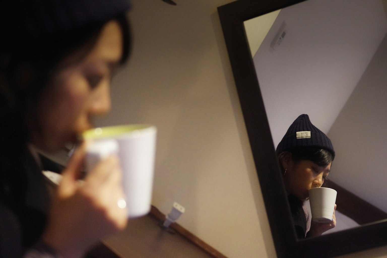 Donna che sorseggia da una tazza in un caffè con il suo riflesso visibile in uno specchio