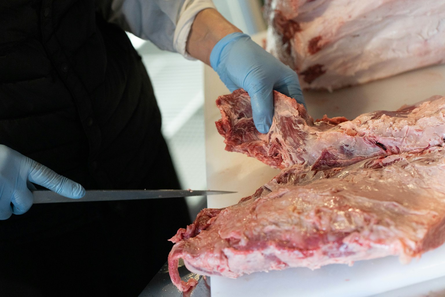 Hände, die ein Messer benutzen, um rohes Fleisch zu schneiden