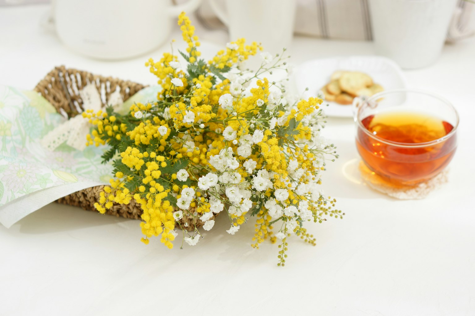 Un arreglo de mesa simple con un ramo de flores amarillas y blancas y una taza de té
