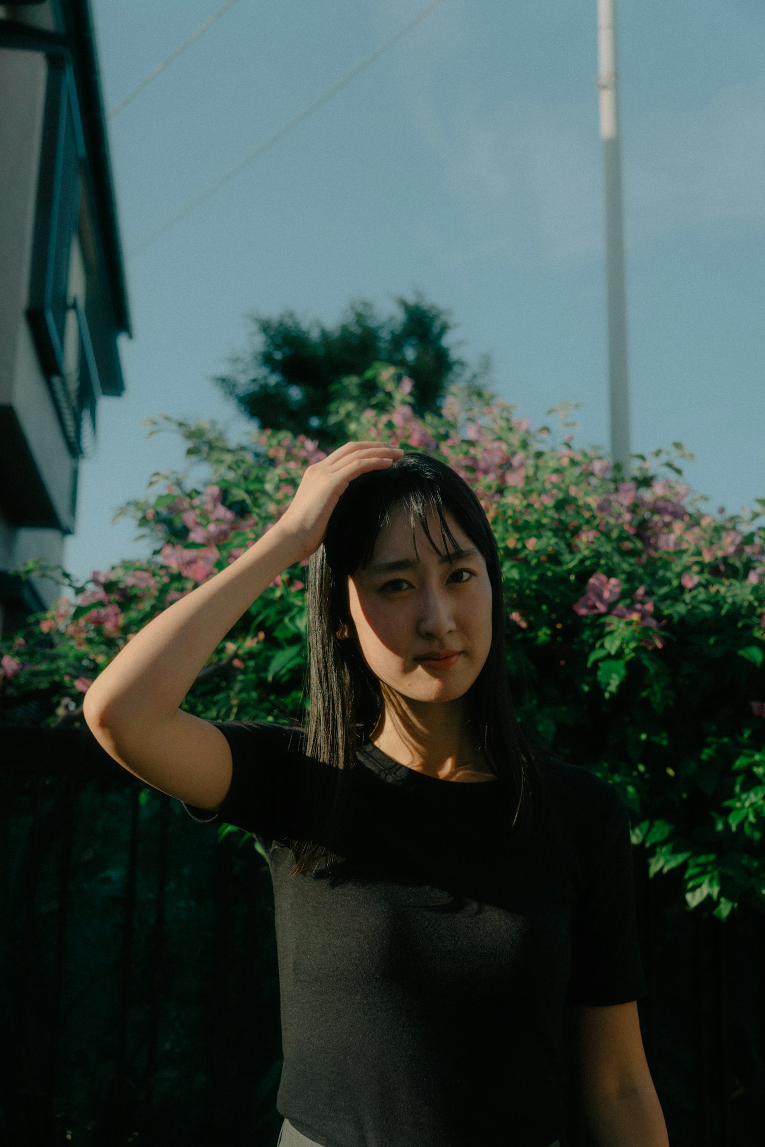 A woman adjusting her hair while looking at the background of flowers and blue sky