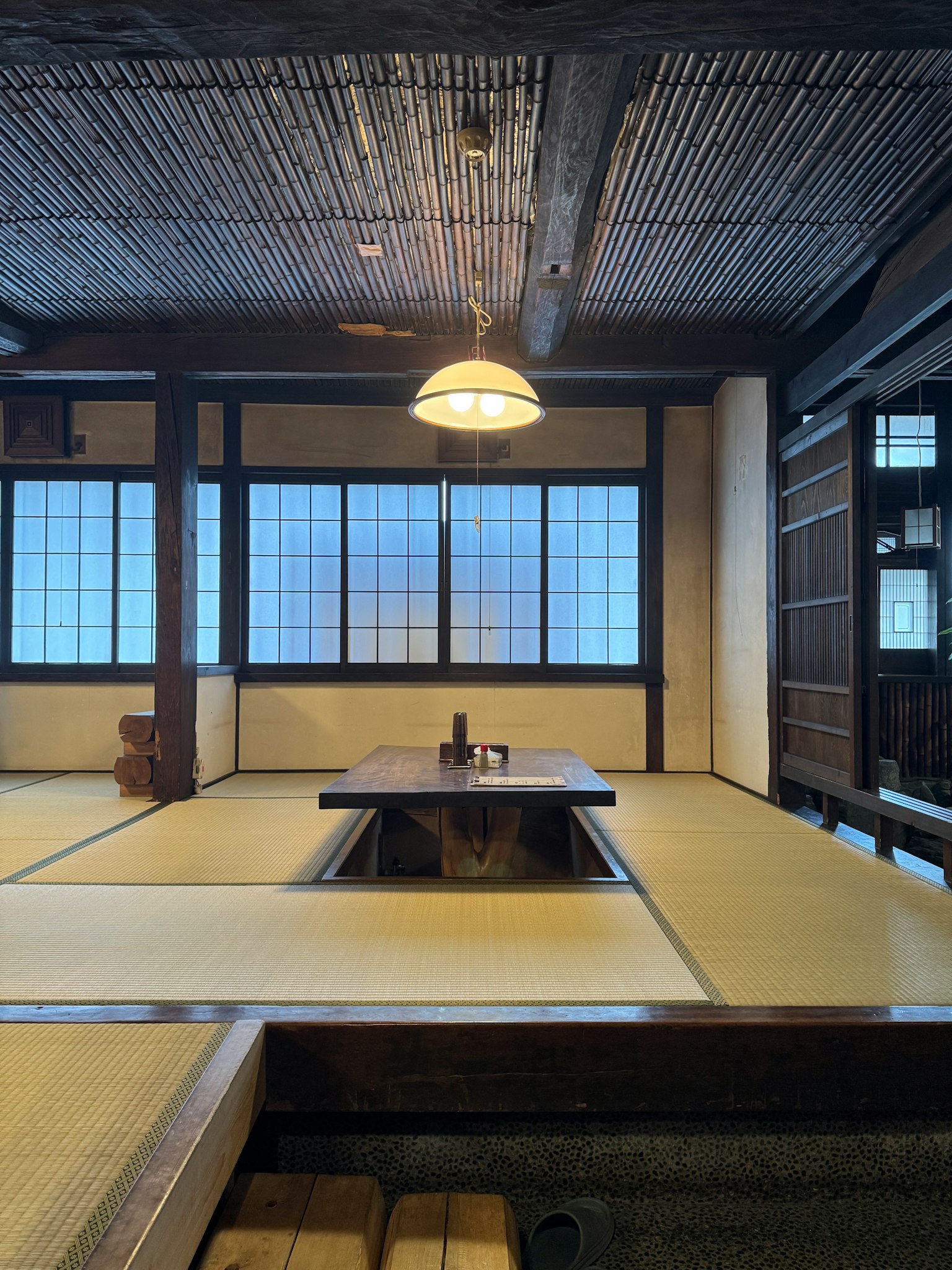 Traditionelles japanisches Hausinterieur mit Tatami Holzbalken Shoji-Fenstern zentralem Tisch und Leuchte